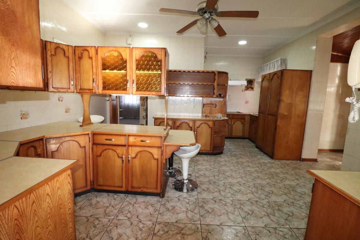Spacious kitchen featuring extensive wooden cabinetry, tiled flooring, and a breakfast bar area, offering significant potential for a modern renovation.