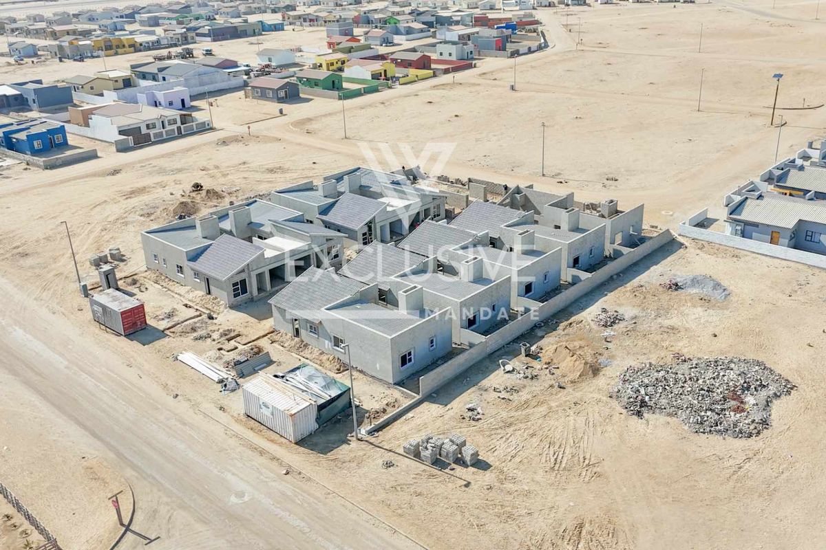 Aerial view of a townhouse development complex under construction, featuring multiple units with tiled roofs and perimeter boundary walls in a desert setting.
