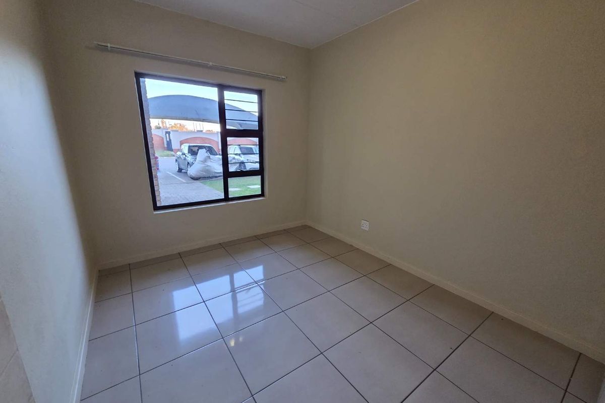 A clean, empty bedroom featuring neutral tiled flooring and a large window providing natural light and a view of the exterior parking area.