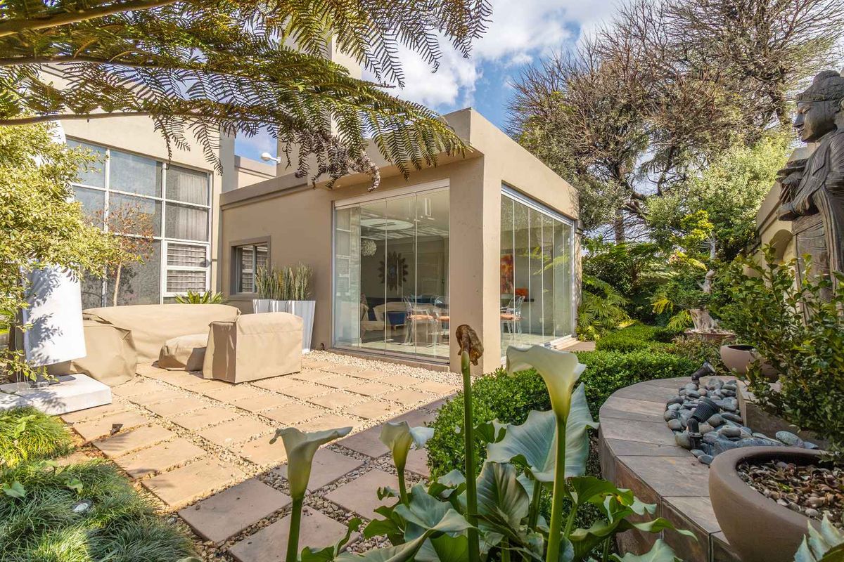 A well-maintained rear garden featuring a paved patio area and a modern glass-enclosed sunroom extension.
