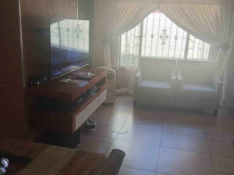 A living room featuring tiled flooring, recessed ceiling lighting, and security bars on the windows, providing a functional and secure living space.