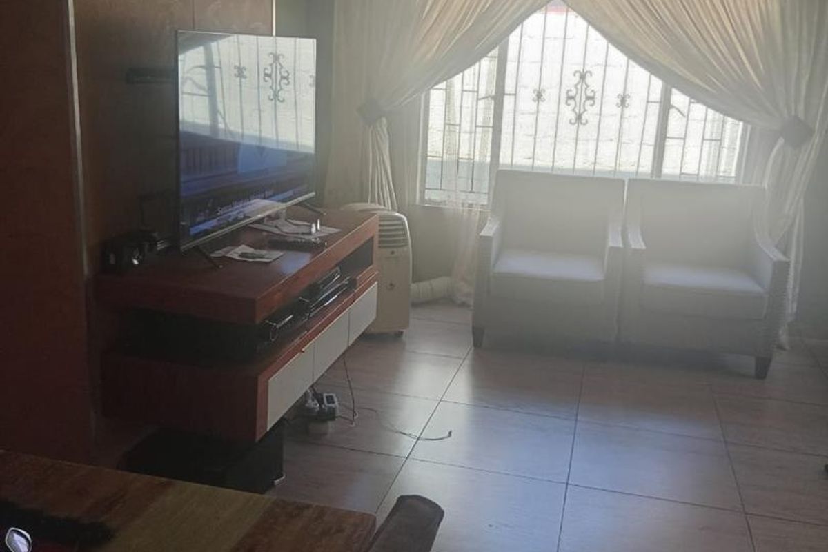 A living room featuring tiled flooring, recessed ceiling lighting, and security bars on the windows, providing a functional and secure living space.