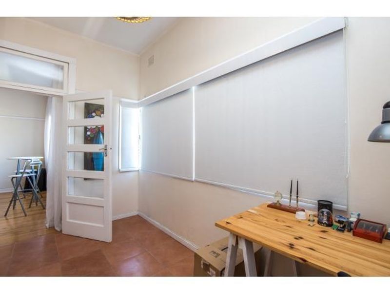 A functional office space featuring tiled flooring, roller blinds, and a classic timber door, providing a bright and versatile work area.