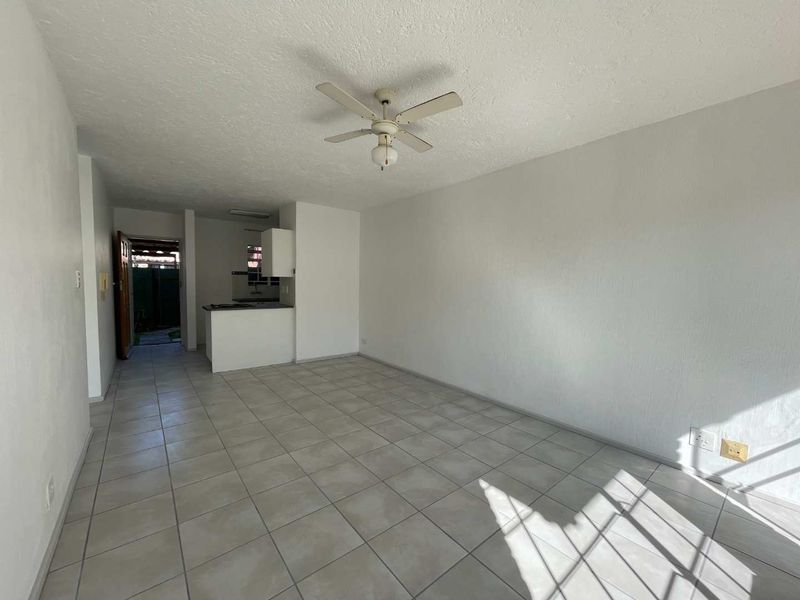 An open-plan living area featuring neutral tiled flooring, a ceiling fan, and a compact kitchen space with built-in cabinetry.