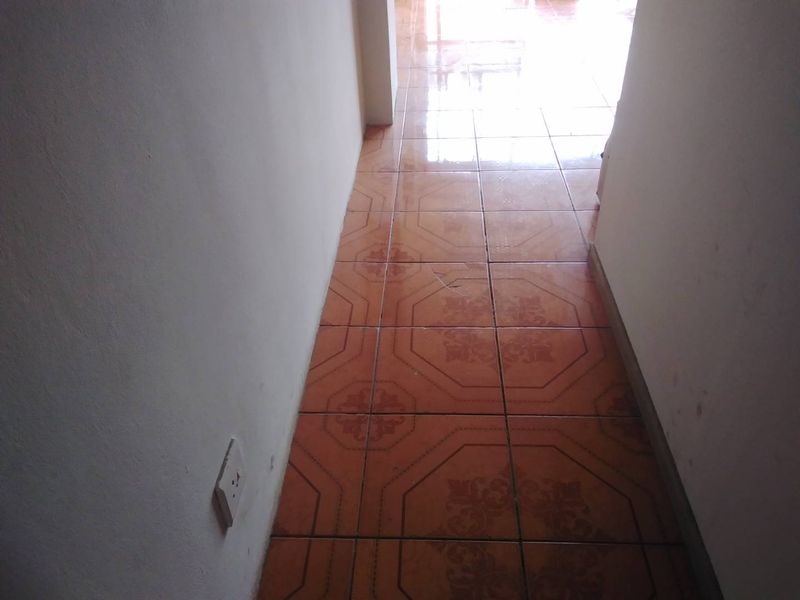 A narrow interior hallway featuring dated ceramic floor tiles and a visible crack in one of the tiles.