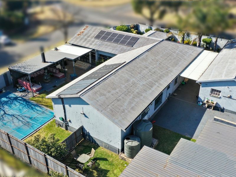 Aerial view of the property featuring a corrugated metal roof with solar panels, a swimming pool with cover, water tanks, and a covered patio area.
