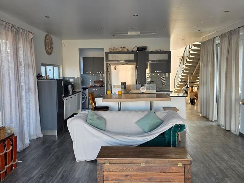 An open-plan living area featuring a modern kitchen with a central island, laminate flooring, and a staircase leading to the upper level.