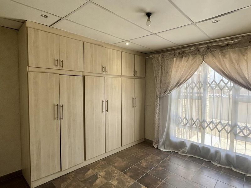 A bedroom featuring extensive built-in wooden cupboards, tiled flooring, and a security gate over the window.