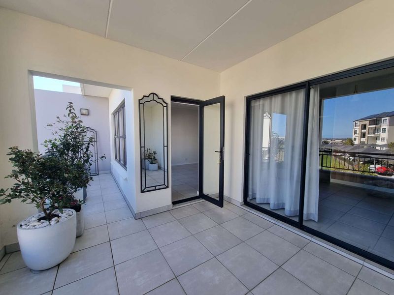 A spacious covered balcony featuring neutral floor tiles and large sliding glass doors providing seamless access to the interior living area.