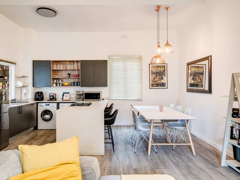 Modern open-plan kitchen and dining area featuring sleek cabinetry, a central island with gas cooktop, integrated laundry, and contemporary pendant lighting.