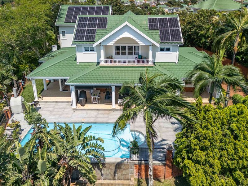 Aerial view of a two-story residential property featuring a green tiled roof with solar panels, a swimming pool, and a covered patio area.