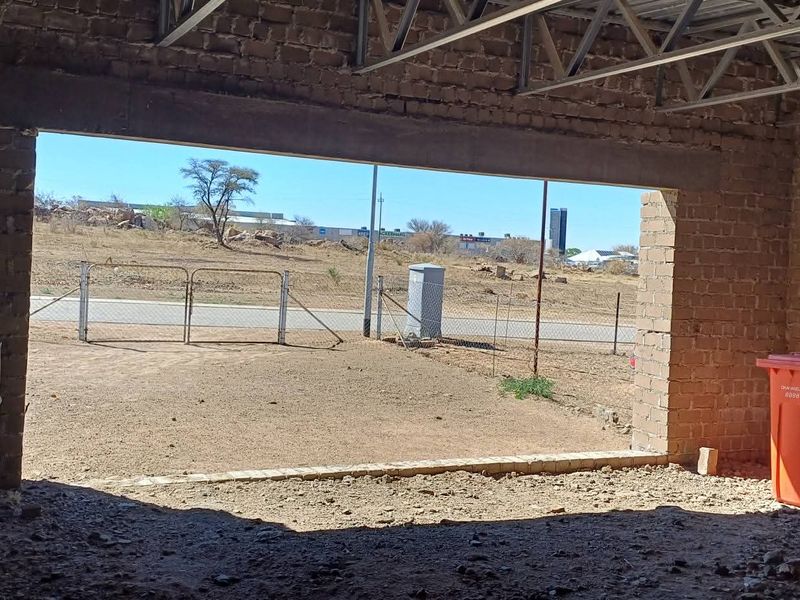 An unfinished garage space featuring exposed brick walls, steel roof trusses, and a dirt floor, currently under construction.