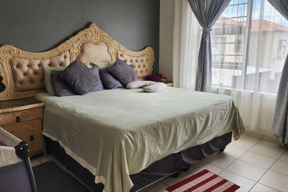A bedroom featuring tiled flooring, a large window with security bars, and a dark accent wall.