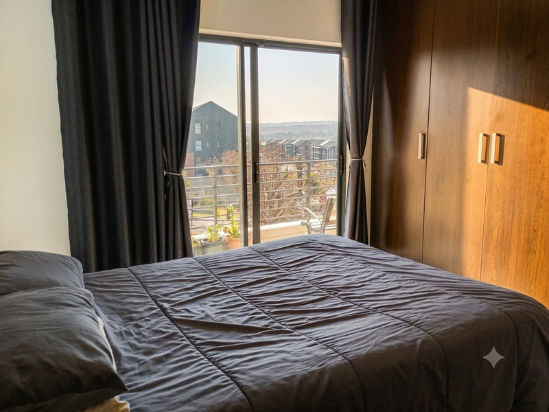 A well-lit bedroom featuring built-in wooden cupboards and a sliding glass door providing access to a private balcony with neighborhood views.