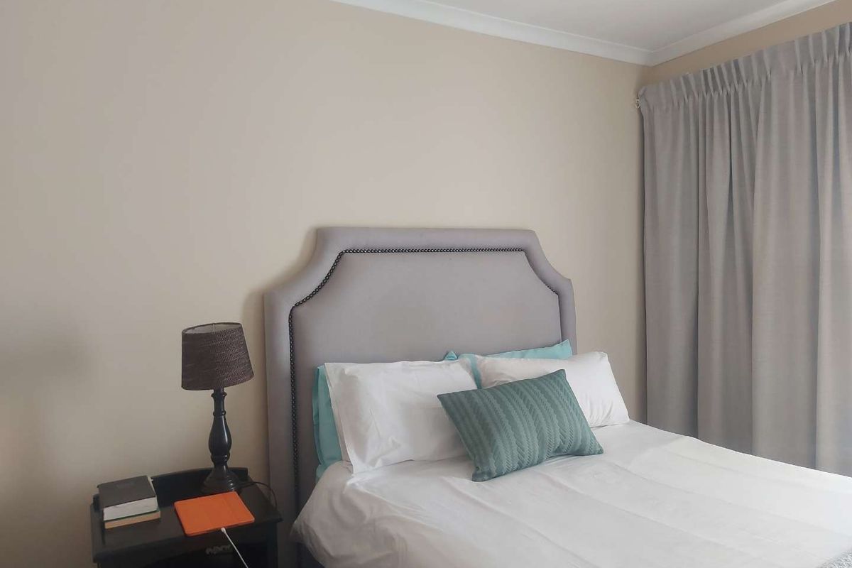 A well-maintained bedroom featuring neutral wall tones, coved ceiling cornicing, and floor-to-ceiling window curtains.