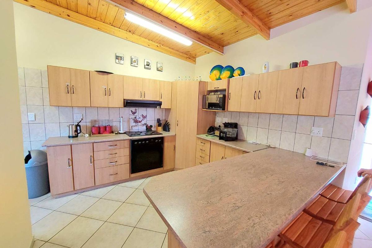 A functional kitchen featuring light wood cabinetry, laminate countertops, a built-in oven and hob, and a breakfast bar with tiled flooring.