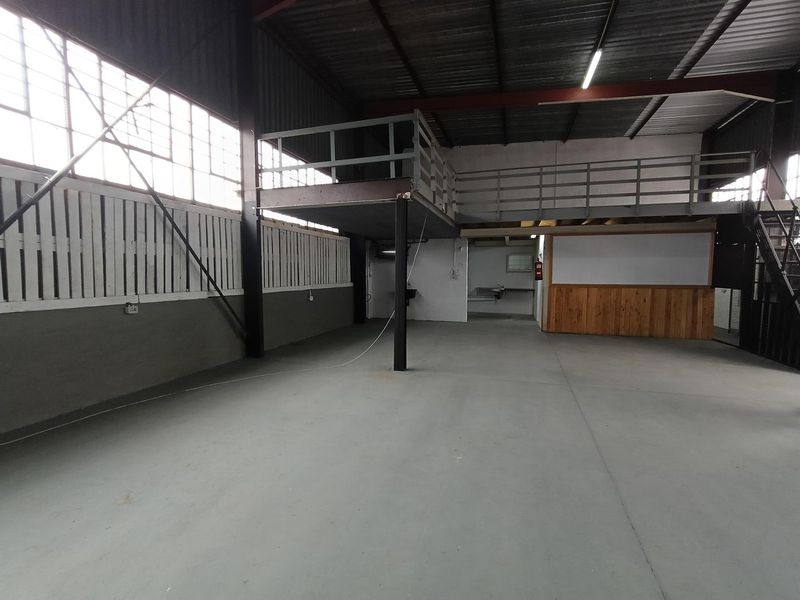 Spacious industrial utility area featuring a mezzanine level, concrete flooring, and high ceilings with exposed steel structural elements.