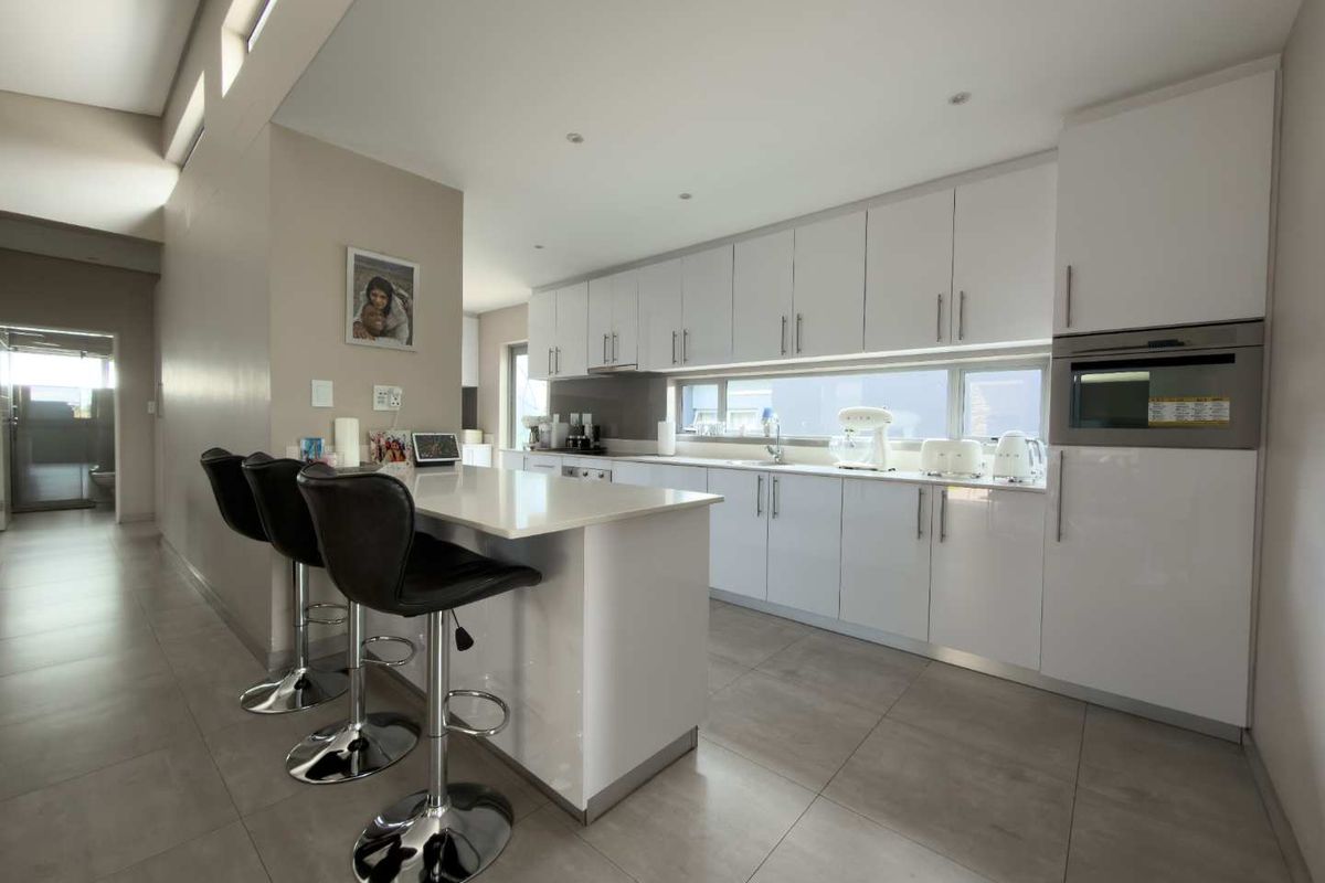 Modern kitchen featuring sleek white cabinetry, stone countertops, a central island with breakfast bar seating, and integrated appliances.