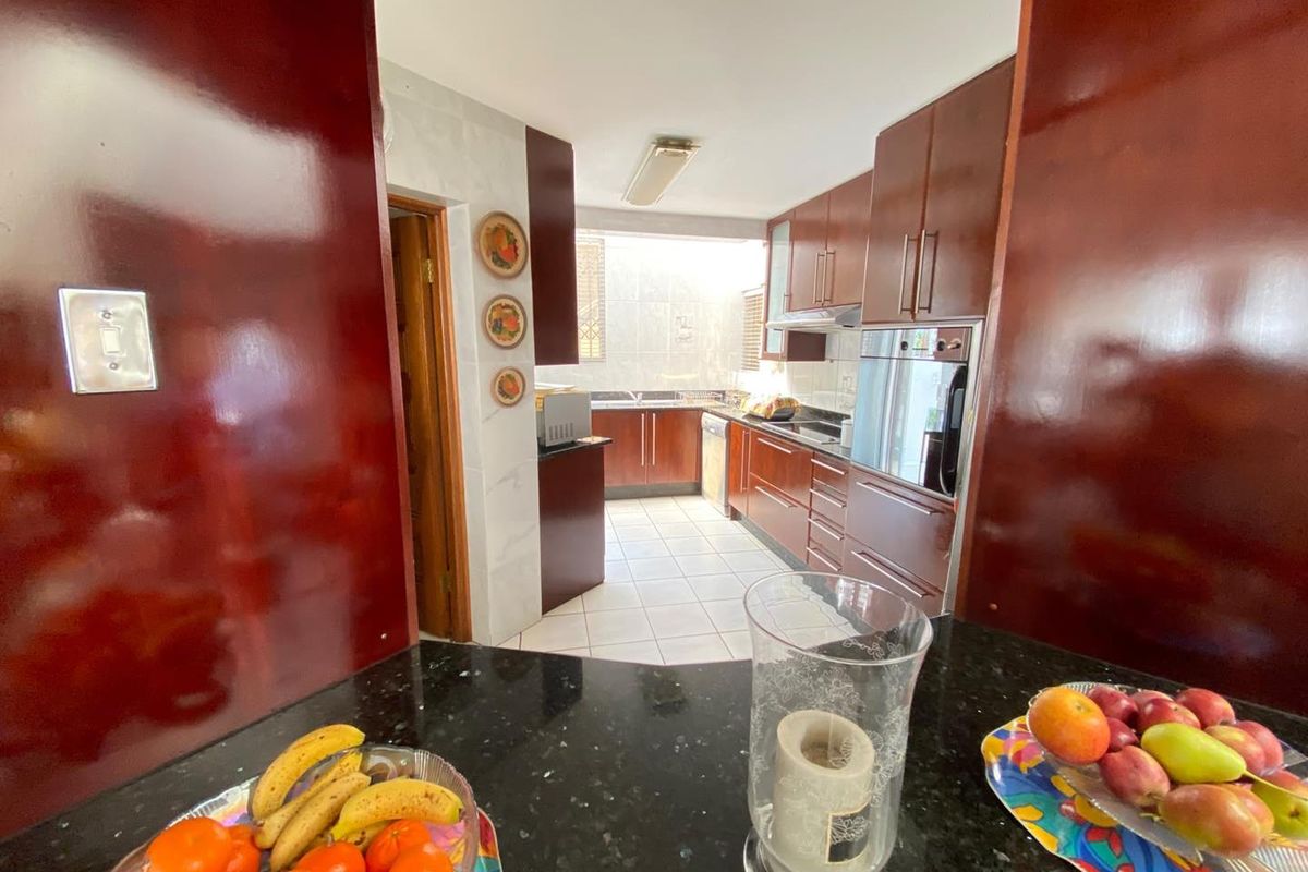 A functional kitchen featuring dark wood cabinetry, granite countertops, built-in oven, extractor fan, and tiled flooring with a practical layout.