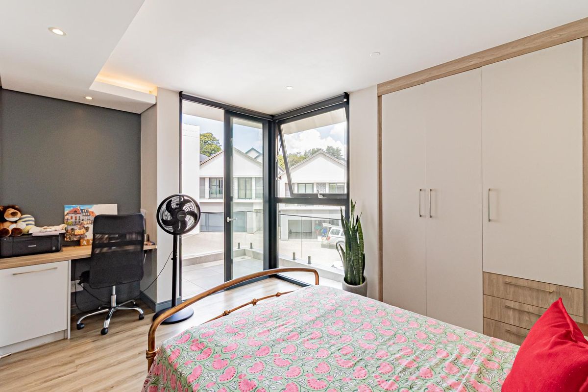 Modern bedroom featuring built-in cabinetry, a dedicated desk area, and large corner windows providing natural light and access to a private balcony.