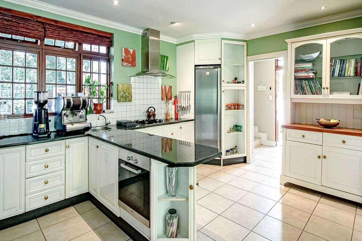 A well-maintained kitchen featuring white cabinetry, dark granite countertops, a built-in oven, stainless steel extractor fan, and tiled flooring.