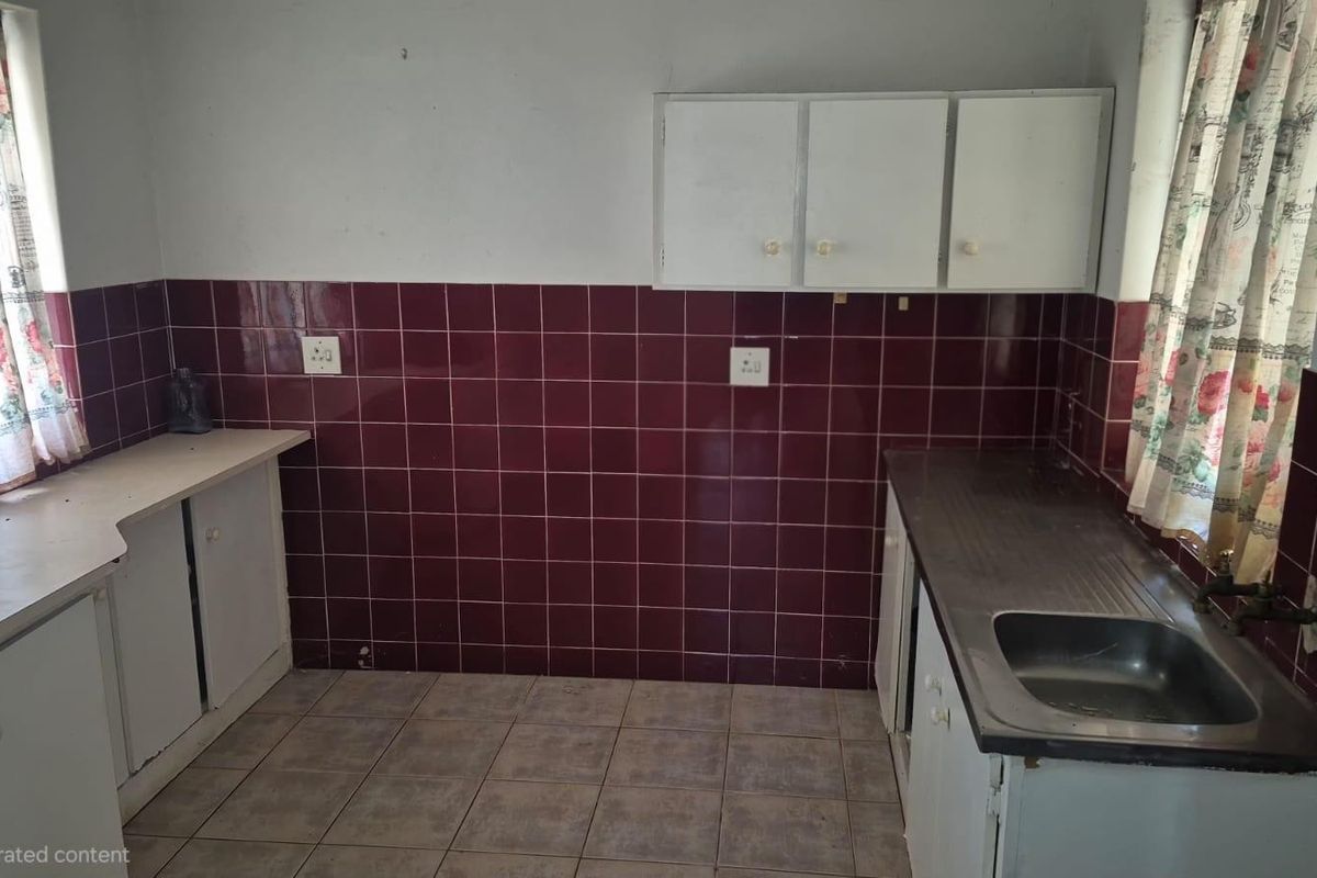 A dated kitchen featuring built-in cabinetry, laminate countertops, a stainless steel sink, and dark tiled splashbacks, offering significant potential for modern renovation.
