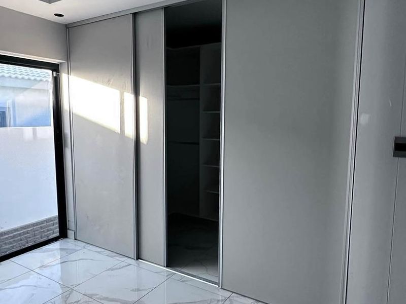 Modern bedroom featuring large-format marble-look porcelain tiles, recessed ceiling lighting, and a sleek built-in sliding door wardrobe with integrated shelving.
