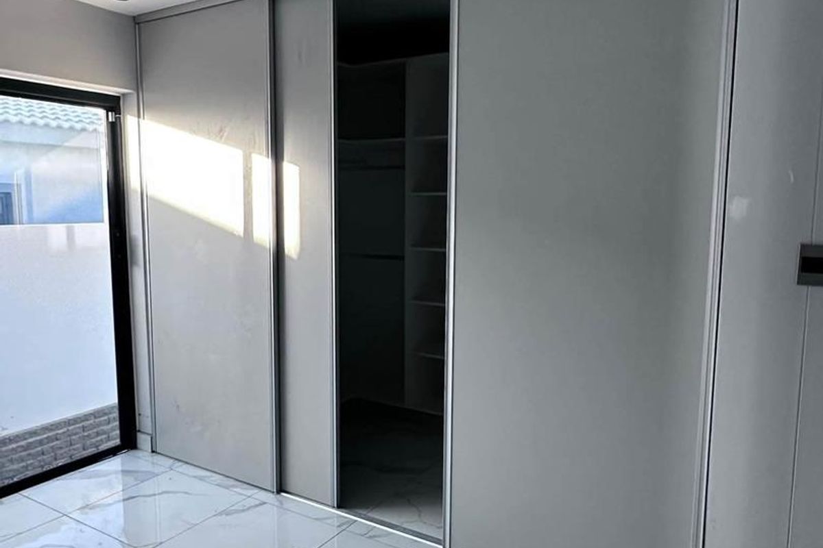 Modern bedroom featuring large-format marble-look porcelain tiles, recessed ceiling lighting, and a sleek built-in sliding door wardrobe with integrated shelving.