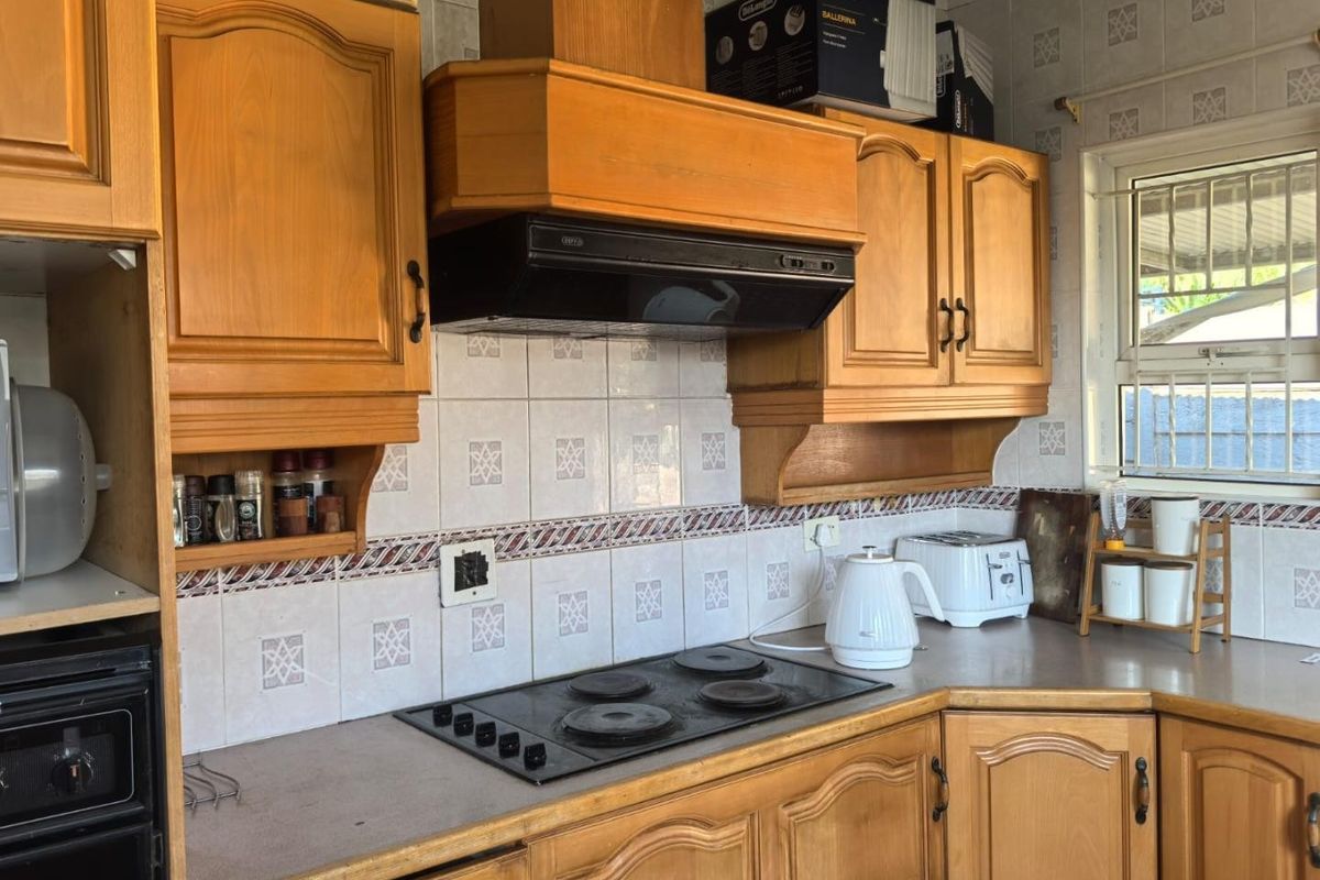 A functional kitchen featuring traditional wooden cabinetry, a tiled backsplash, and a built-in electric hob with an extractor fan.
