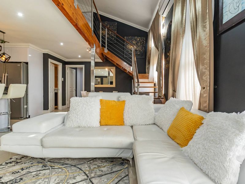Modern open-plan living area featuring a striking timber staircase, sleek kitchen cabinetry, and high-quality finishes throughout this well-maintained apartment space.