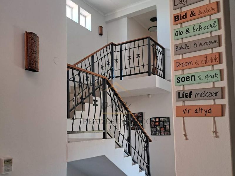 A bright, double-volume entrance hallway featuring a staircase with a decorative wrought iron railing and wooden handrail.