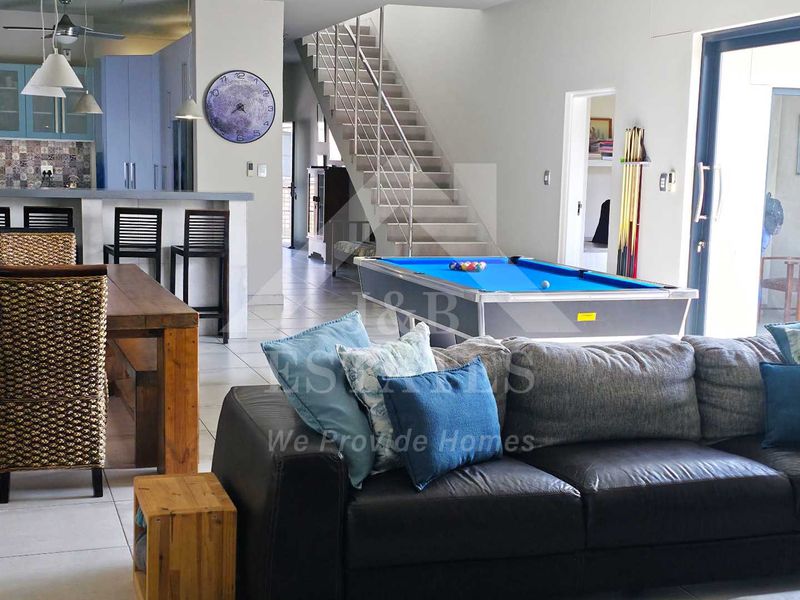 Spacious open-plan living area featuring a modern kitchen with island, tiled flooring, and a staircase leading to the upper level with sliding door access.