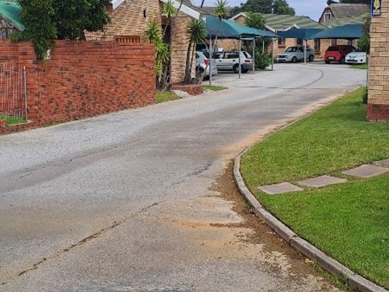 A view of the townhouse complex driveway featuring brick boundary walls, paved access roads, and covered carport parking areas.