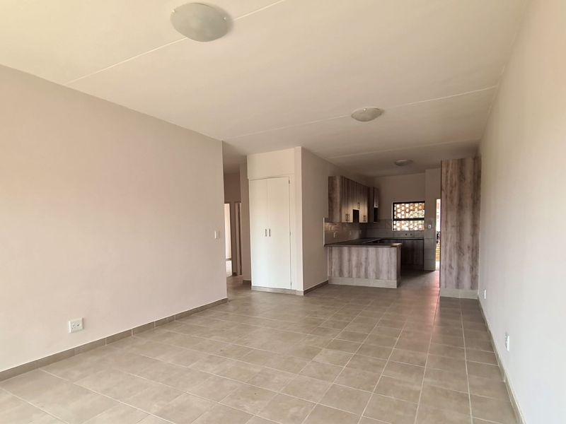 An open-plan living and kitchen area featuring neutral tiled flooring, built-in cabinetry, and a clean, minimalist layout ready for personalization.