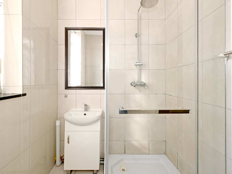 A functional bathroom featuring a shower enclosure, vanity basin, and wall-mounted mirror with neutral tiled finishes.