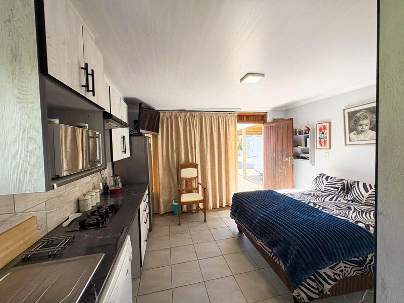 Open-plan studio space featuring a compact kitchenette with built-in cabinetry, gas hob, and tiled flooring, with direct access to an outdoor area.