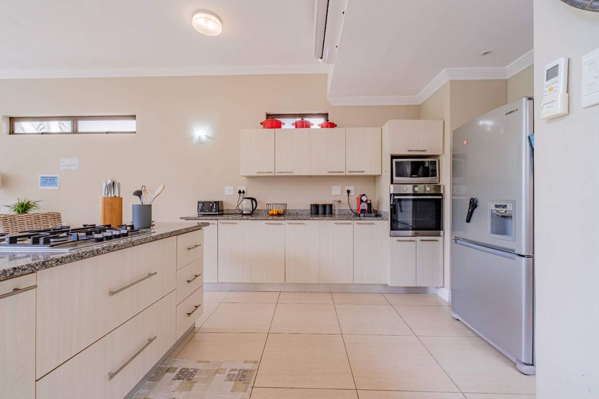 Modern kitchen featuring light wood cabinetry, granite countertops, a central island with a gas hob, and built-in oven and microwave.