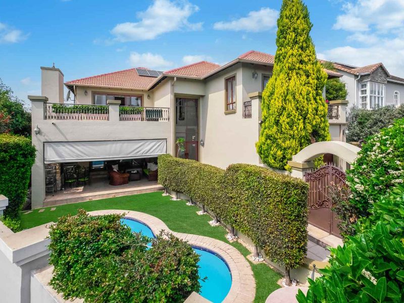 Rear view of the property featuring a swimming pool, landscaped garden, covered patio area, and an upper-level balcony with wrought iron railings.