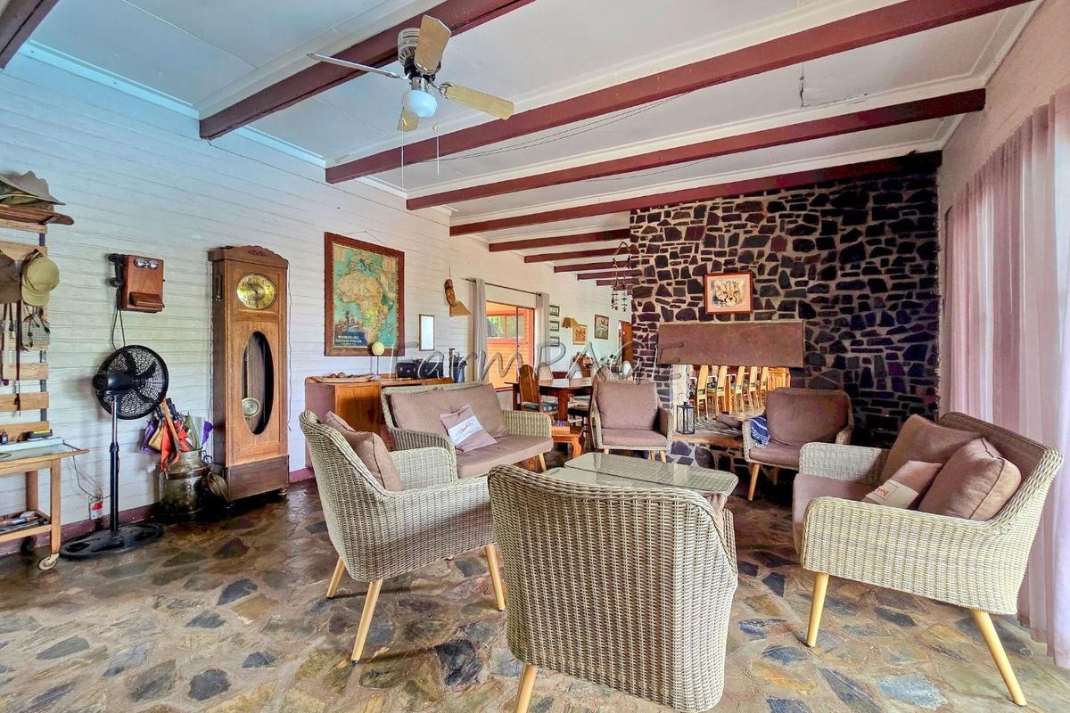 Spacious living area featuring exposed timber ceiling beams, a prominent natural stone fireplace, and rustic stone flooring.