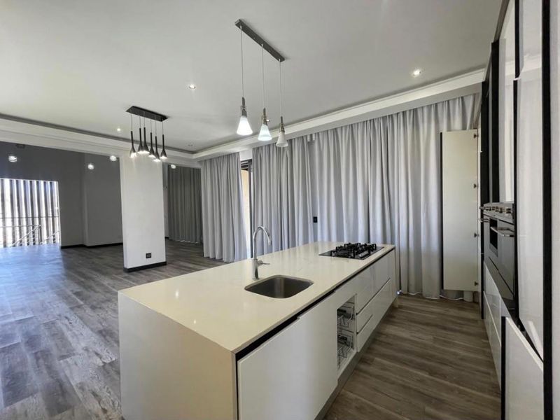 Modern open-plan kitchen featuring a central island with a gas hob, built-in oven, and sleek cabinetry, seamlessly flowing into the living area.