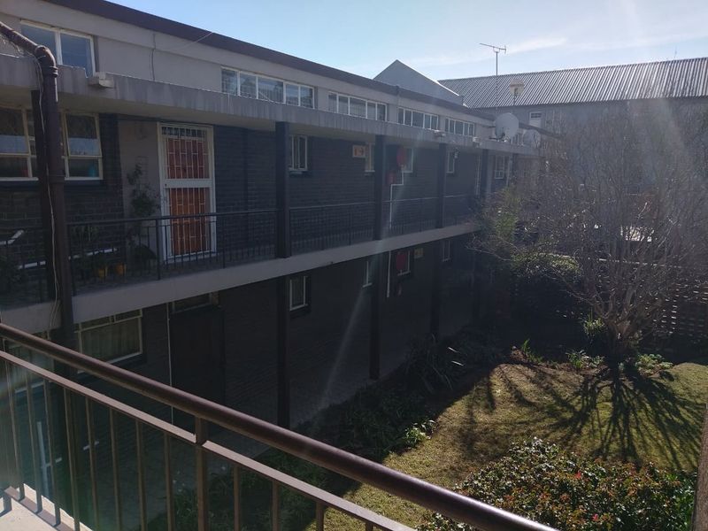 Rear view of a multi-story townhouse complex featuring brick facade, metal balcony railings, and a shared garden area.