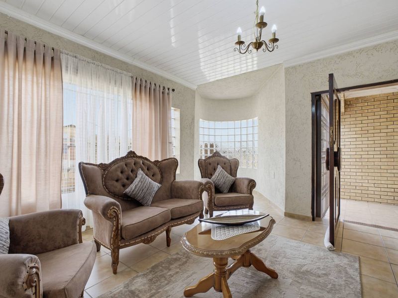 A bright living room featuring tiled flooring, a unique glass block window, and a classic tongue and groove ceiling with a central chandelier.