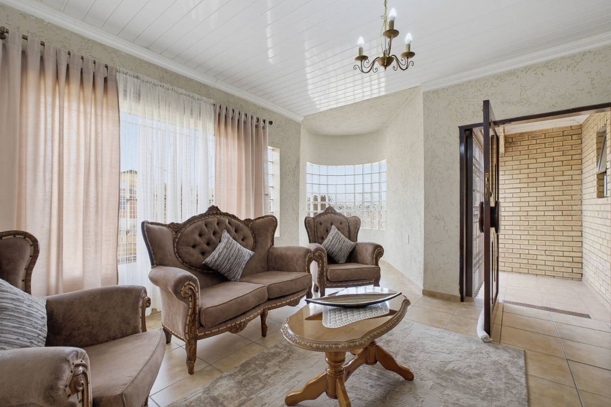 A bright living room featuring tiled flooring, a unique glass block window, and a classic tongue and groove ceiling with a central chandelier.