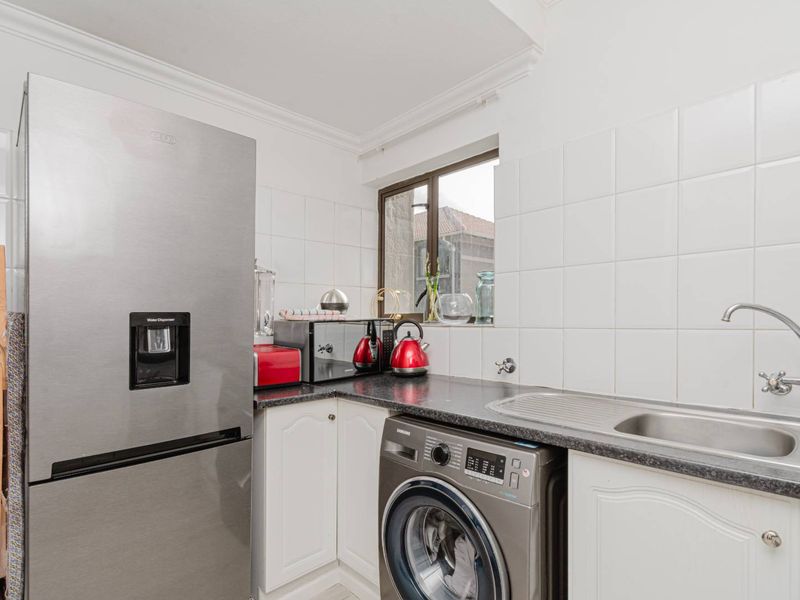Compact kitchen featuring white cabinetry, dark laminate countertops, tiled splashbacks, and a stainless steel sink with a mixer tap.