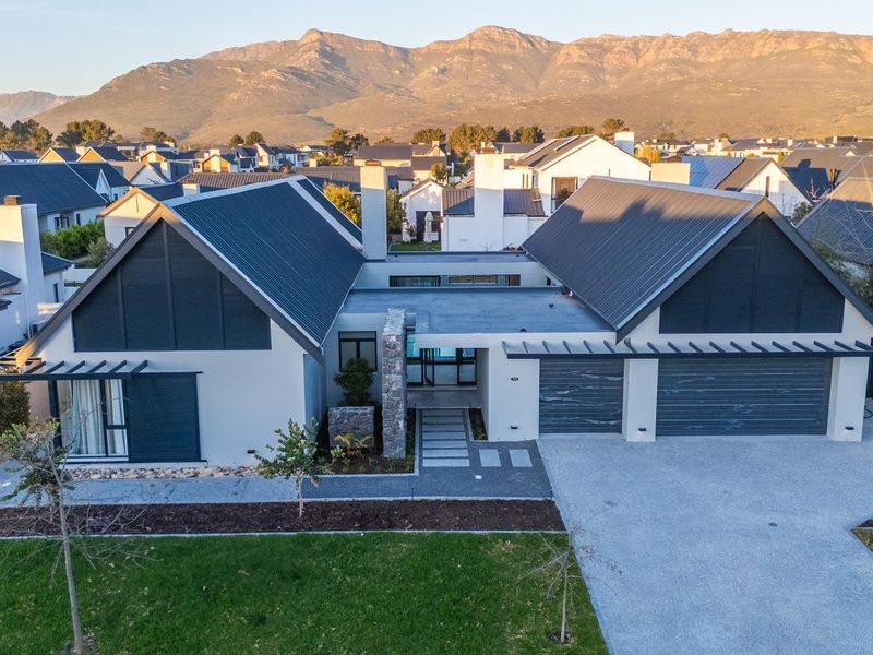 Aerial view of a modern residential property featuring a double garage, metal roofing, stone accents, and a well-maintained garden against a mountain backdrop.