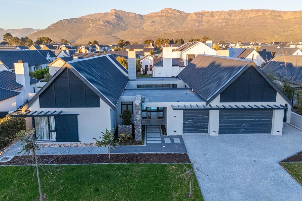 Aerial view of a modern residential property featuring a double garage, metal roofing, stone accents, and a well-maintained garden against a mountain backdrop.