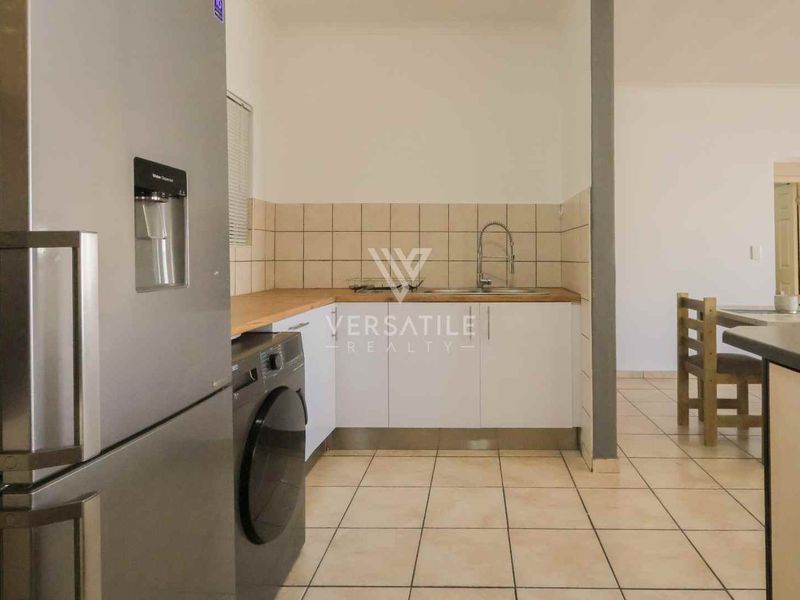 A functional kitchen featuring tiled flooring, a neutral backsplash, built-in cabinetry, and a stainless steel sink with a modern faucet.
