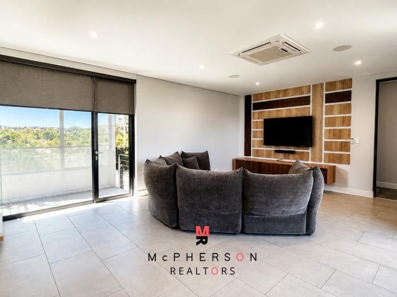 Modern living room featuring tiled floors, ducted air conditioning, and a stylish timber feature wall with integrated media storage and balcony access.