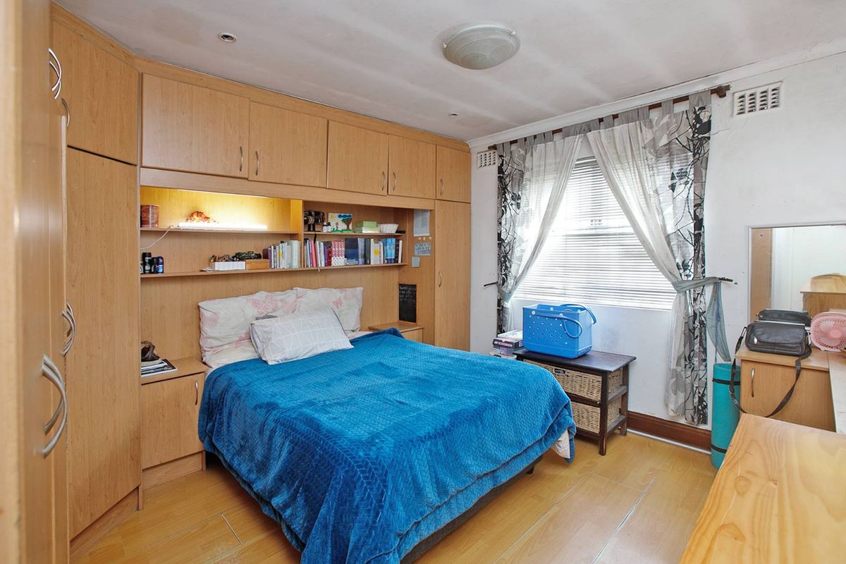 A bedroom featuring extensive built-in wooden cabinetry and shelving surrounding the bed area, with laminate flooring and a window with integrated blinds.