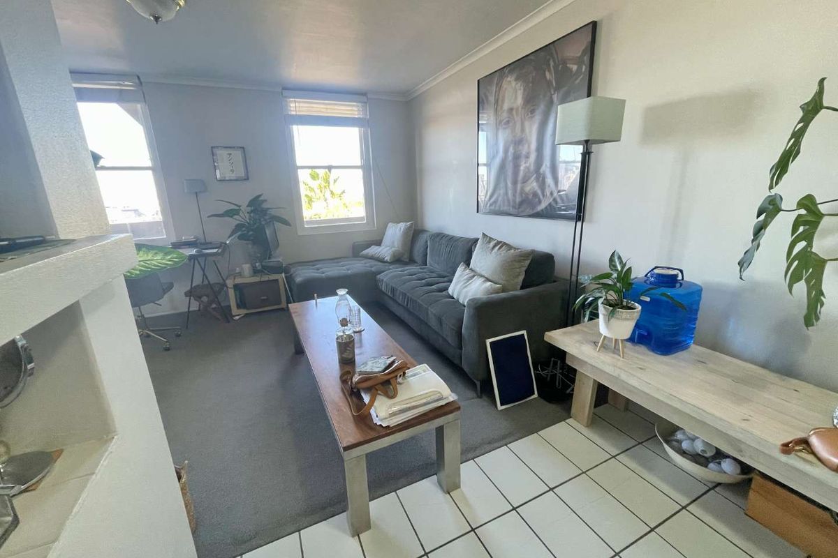 A living room area featuring a combination of tiled and carpeted flooring, with natural light entering through two windows.